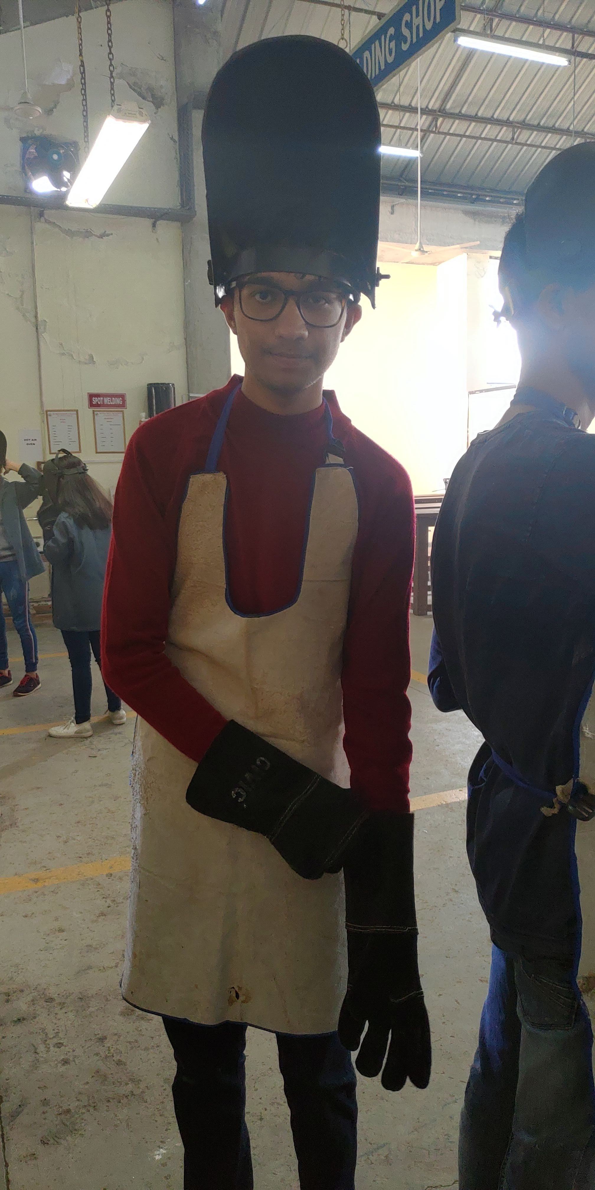 Naman in red sweater, leather apron and welding helmet at the engineering workshop, first year