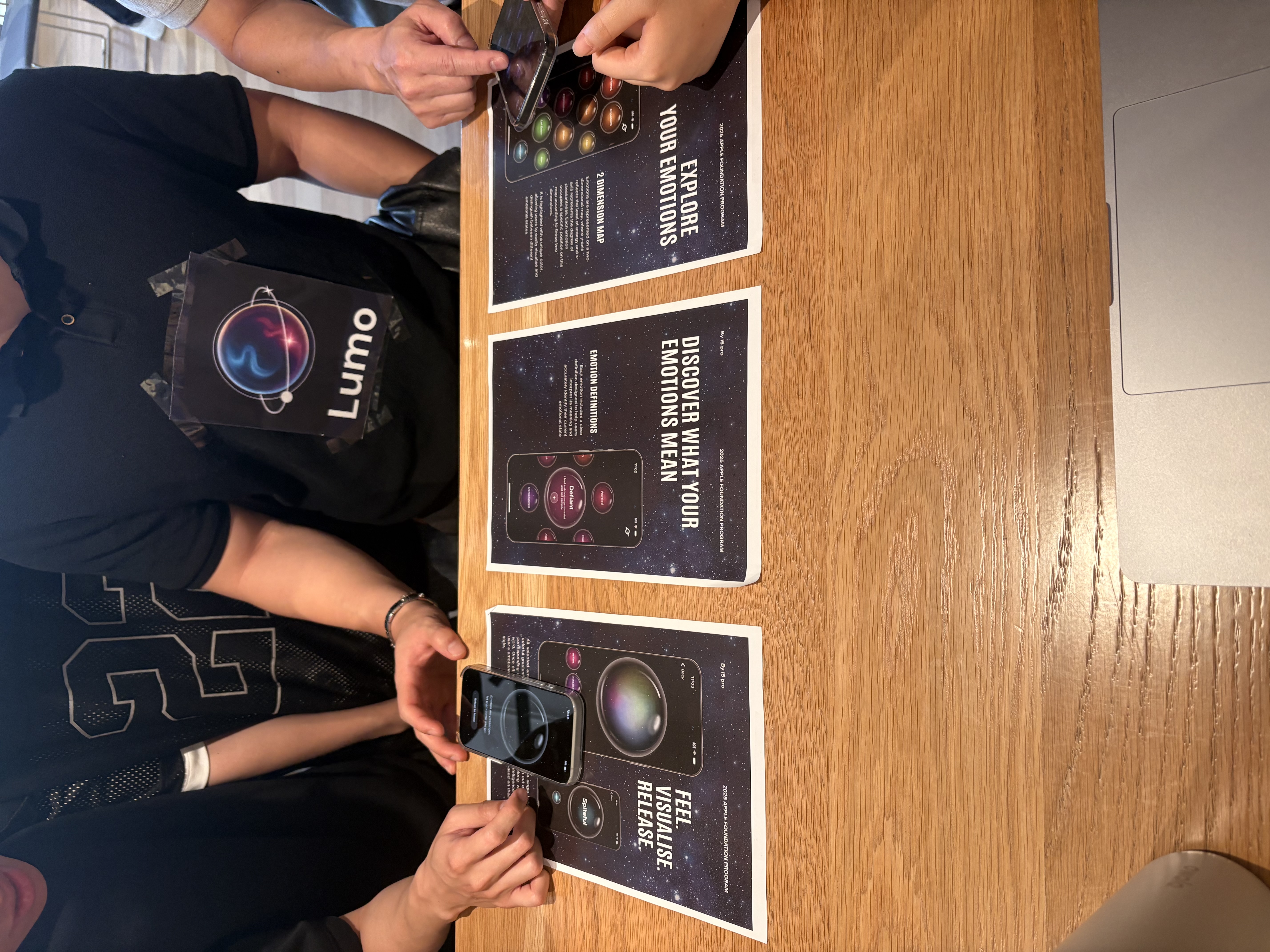 Team i5 Pro at their demo day table with printed Lumo marketing materials, testing the app on phones